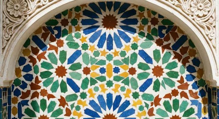 Zellige tilework close-up from Morocco — the hand-cut ceramic tiles arranged in geometric patterns that are the direct Moroccan continuation of the Andalusian tile tradition, made by craftsmen in Fes using techniques unchanged for five centuries